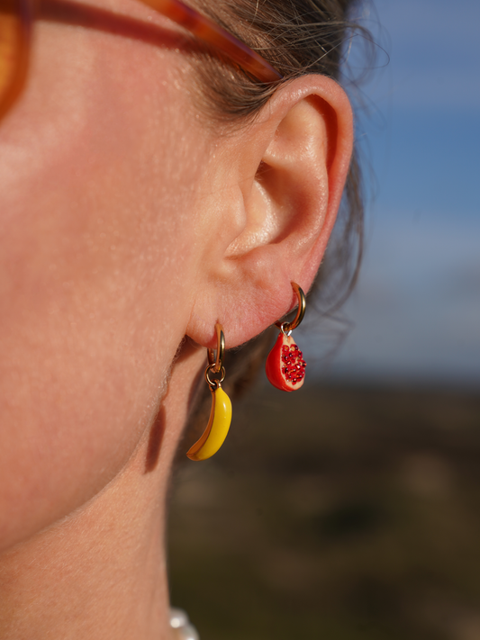 Close-up of a person wearing colorful earrings with a blurred natural background