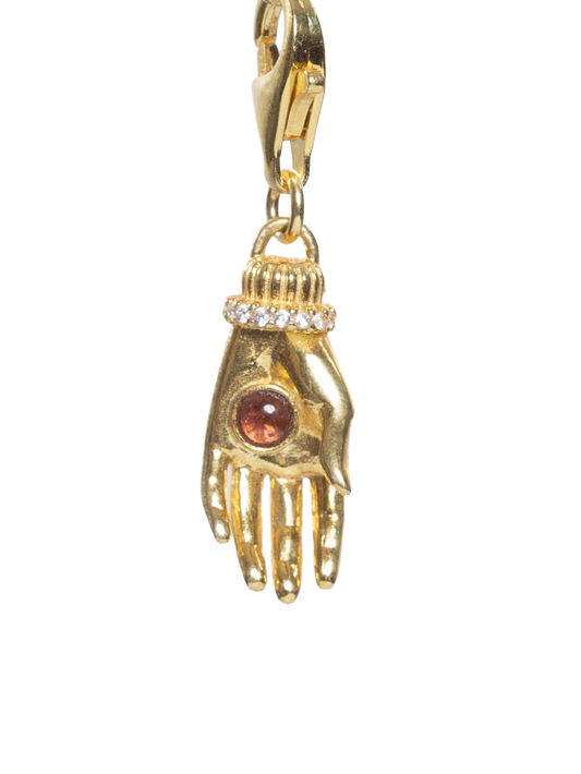 Gold charm shaped like a hand with a brown gemstone on a white background
