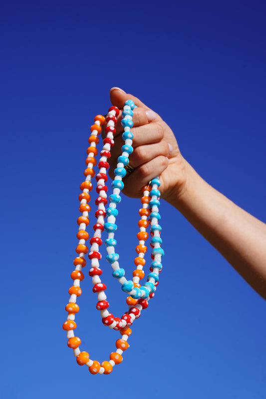 Hand holding colorful bead mushroom necklaces against a clear blue sky