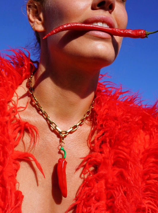 Person wearing a red feathered garment and gold chain with a chili pepper pendant, holding a red chili pepper.