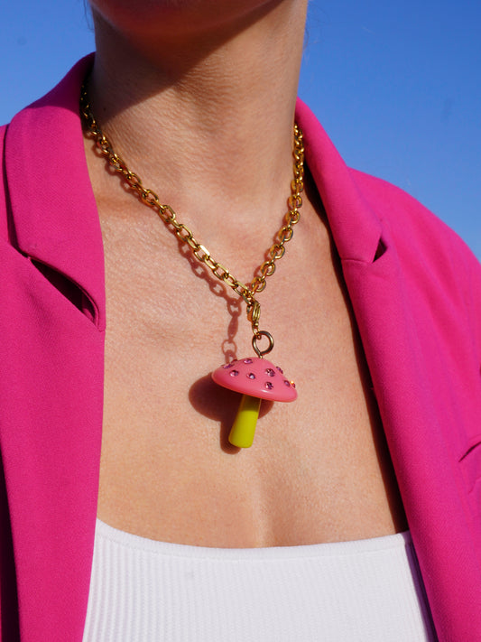 Necklace with a pink glitter mushroom pendant worn by a person against a pink background