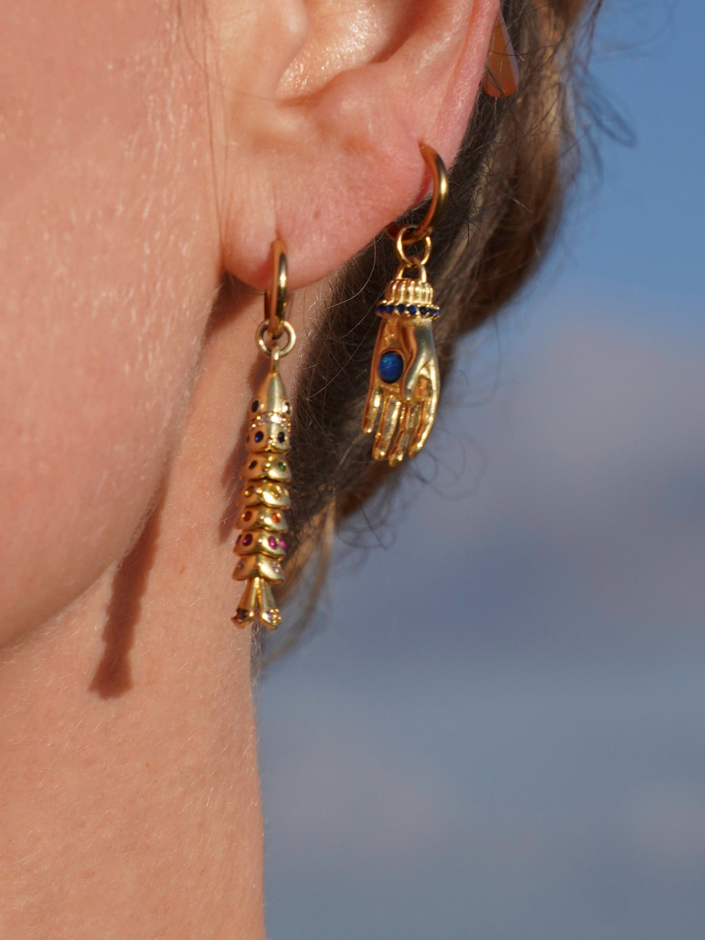 Close-up of a person wearing gold hoop earrings with blue stones against a blurred background