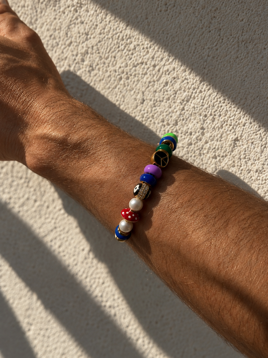 A multicolor beaded MILLIE MADNESS Bracelet worn on a person's wrist, photographed outdoors against a textured beige wall with strong natural shadows.