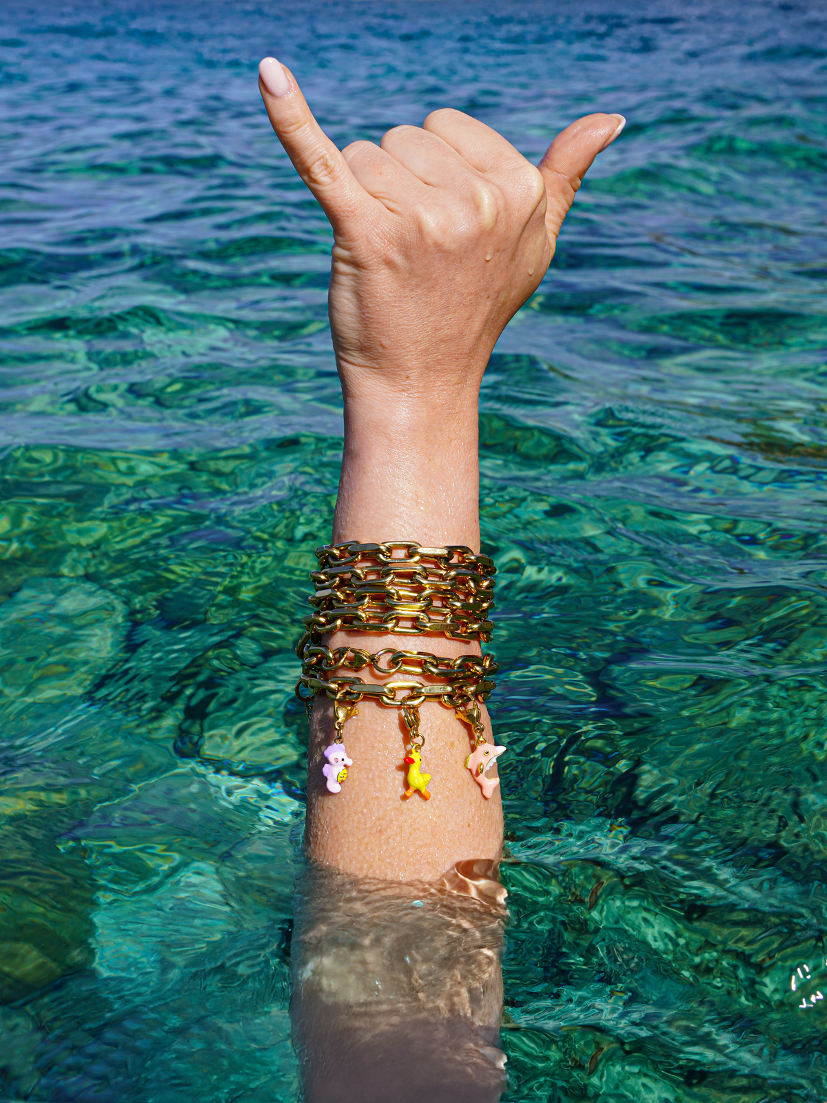 Hand making a 'hang loose' sign with gold bracelets in clear blue water