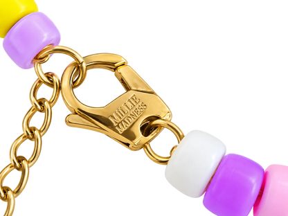 Close-up of a gold-tone chain bracelet with a lobster clasp engraved with 'MILLIE MADNESS' and colorful round beads in yellow, lavender, white, and pink on a white background.