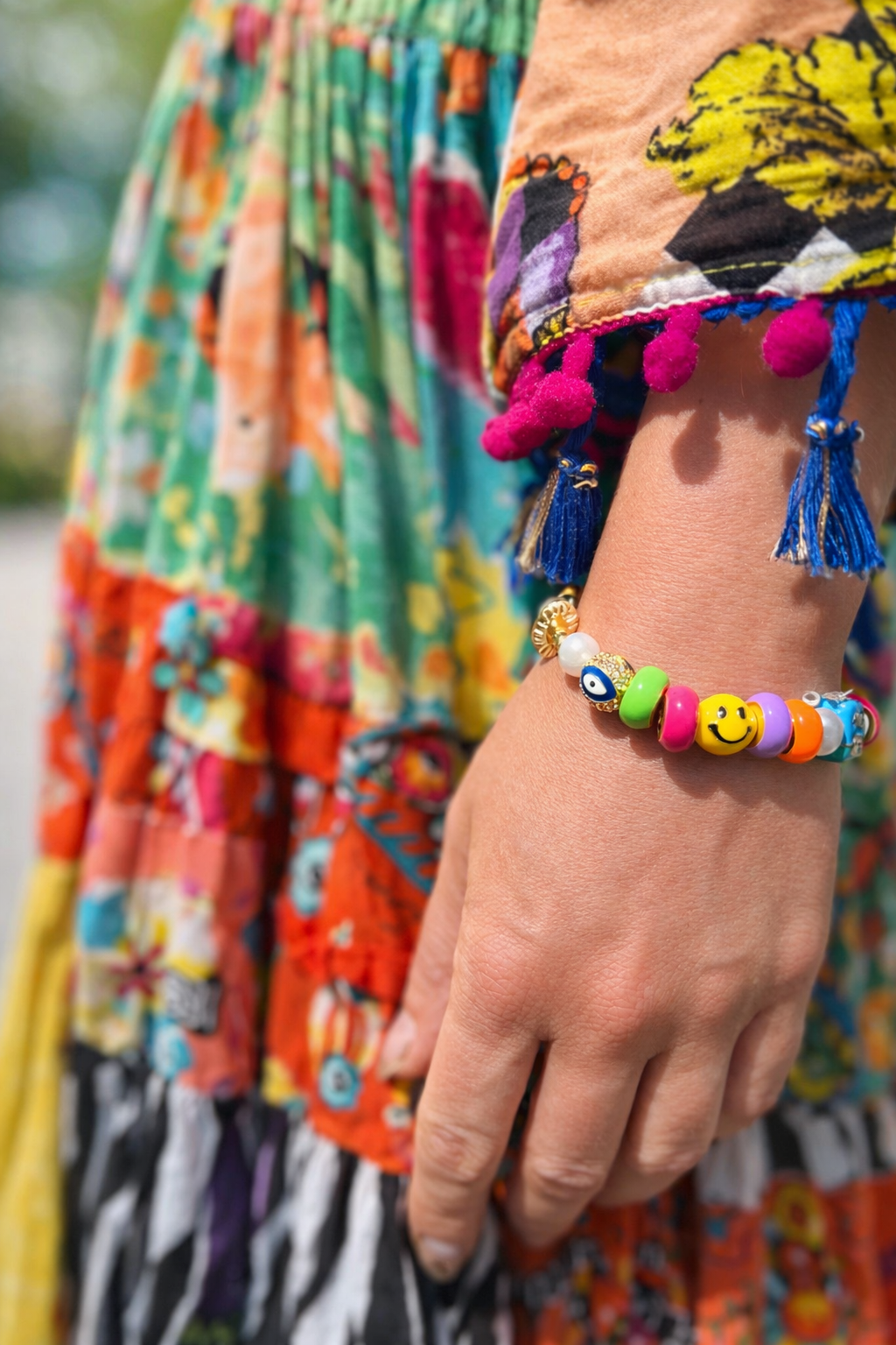 Colorful bracelet with smiley face charms worn on a wrist against a multicolored fabric background.