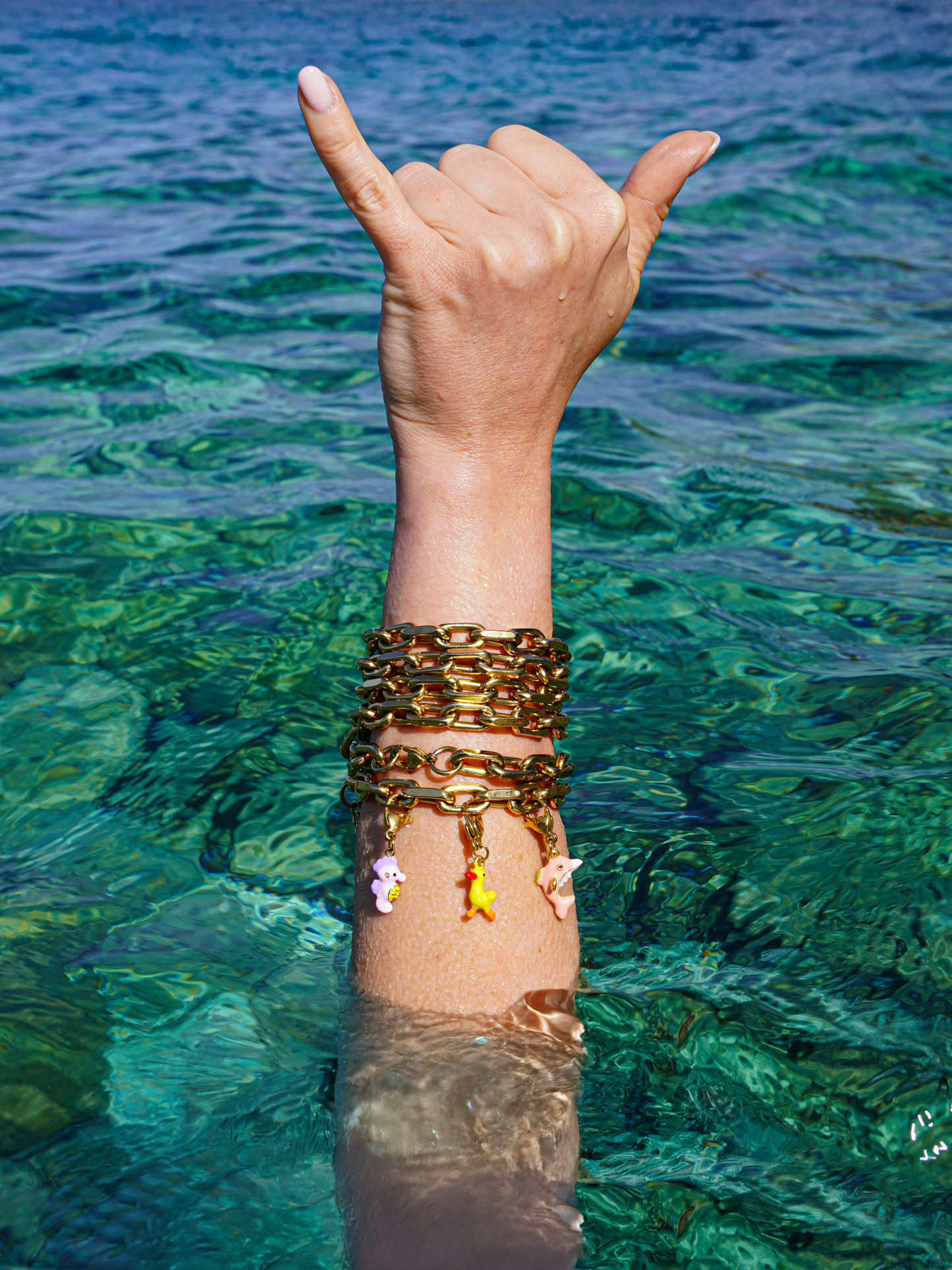 Hand making a 'hang loose' sign with gold bracelets in clear blue water