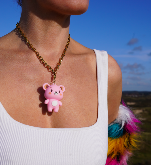 Person wearing a necklace with a pink bear pendant against a blue sky.