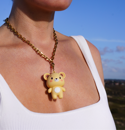 Person wearing a gold chain necklace with a bear pendant against a blue sky.