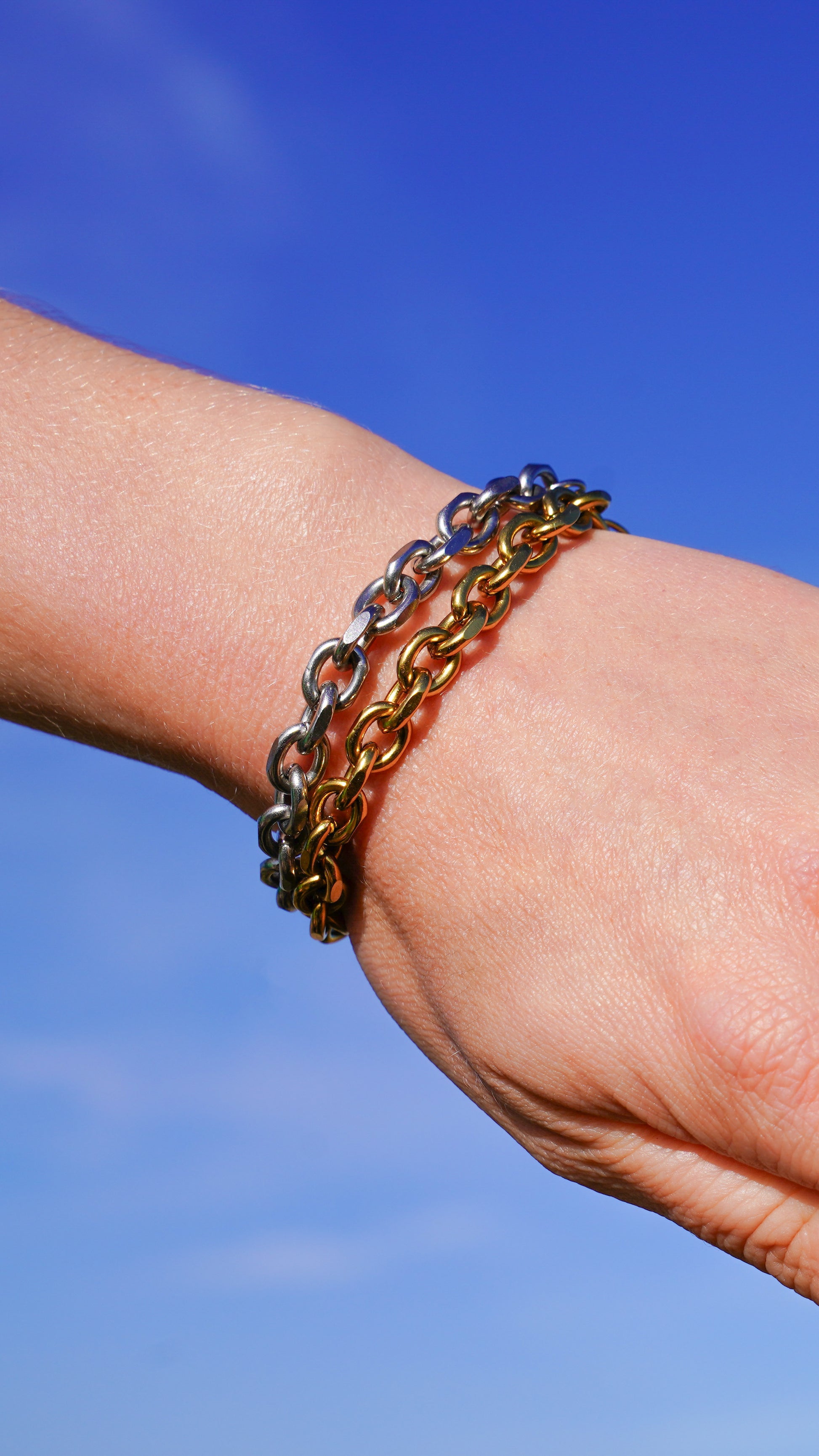 Close-up of a wrist wearing multiple chain bracelets against a blue sky.