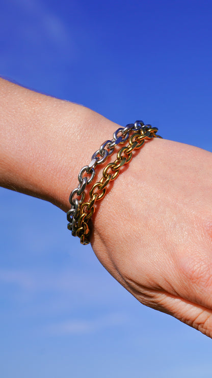 Close-up of a wrist wearing multiple chain bracelets against a blue sky.