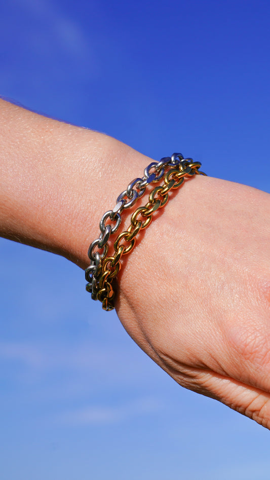 Close-up of a wrist wearing multiple chain bracelets against a blue sky.