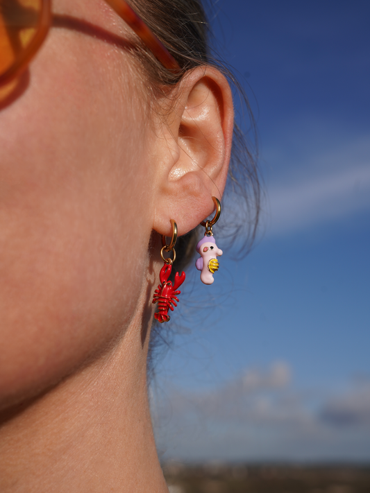 Close-up of an ear wearing two earrings of a lobster earring and a seahorse earring with a clear blue sky background
