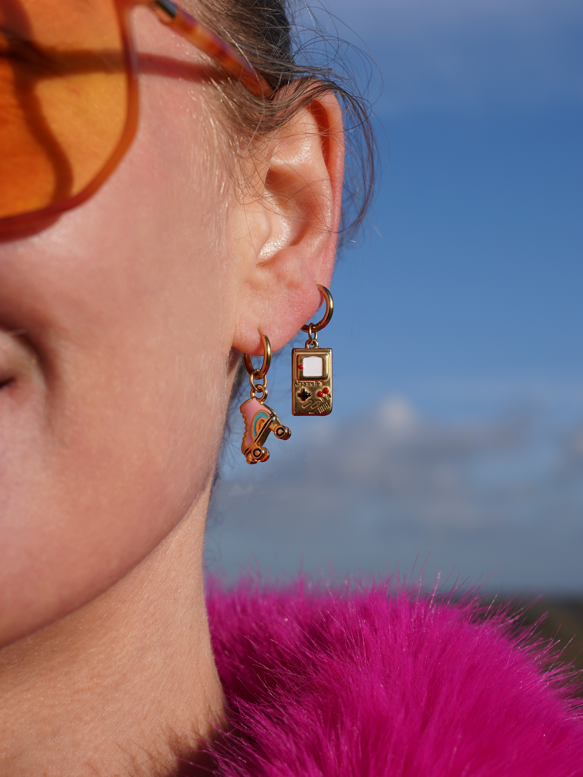 Close-up of a person wearing colorful earrings with a rollerskate and a game boy with a blurred background