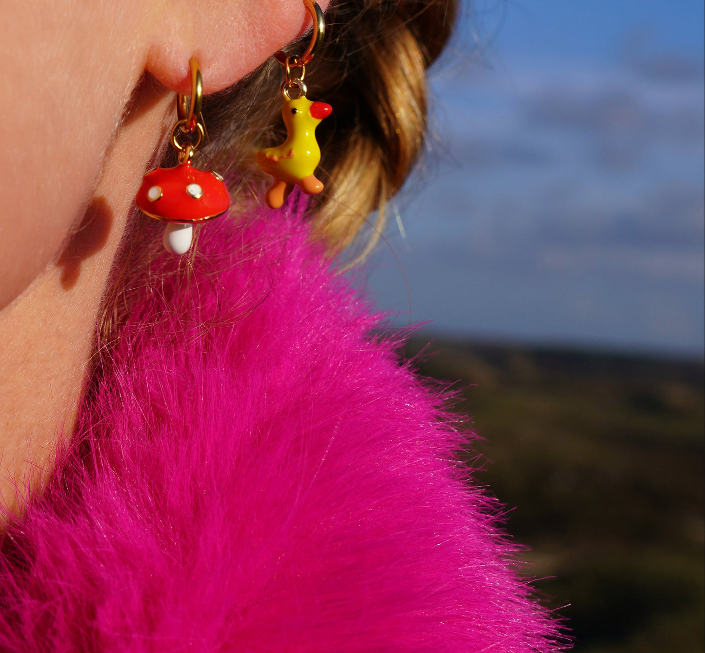 Close-up of a person wearing colorful earrings with a blurred natural background
