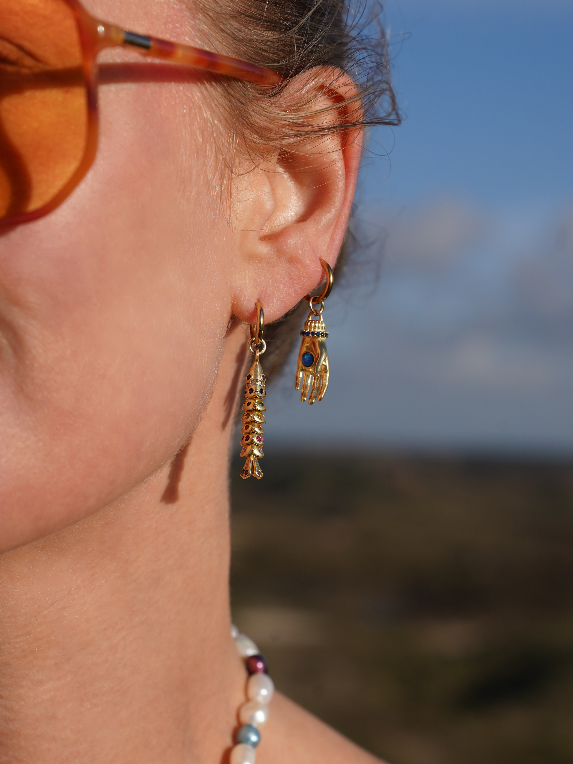 Close-up of a person wearing gold earrings with a blurred natural background
