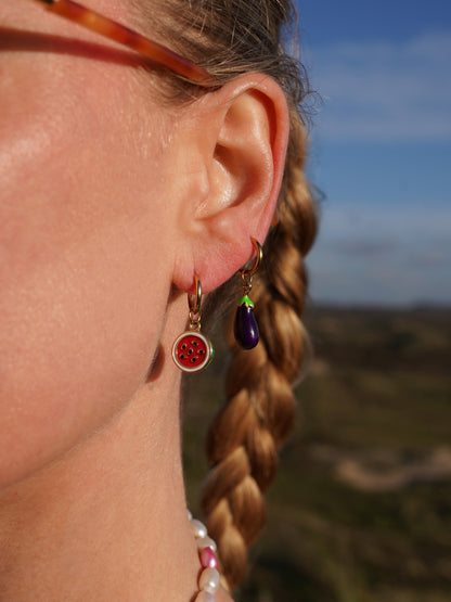 Close-up of a person's ear with earrings, watermelon earring and an aubergine earring, blurred natural background