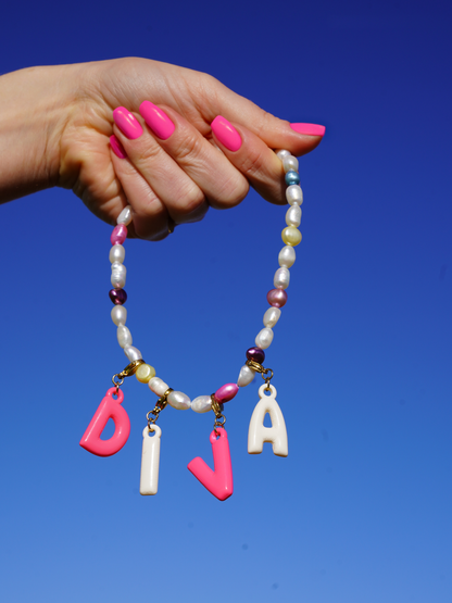 Hand holding a beaded necklace with colorful letter charms against a blue sky