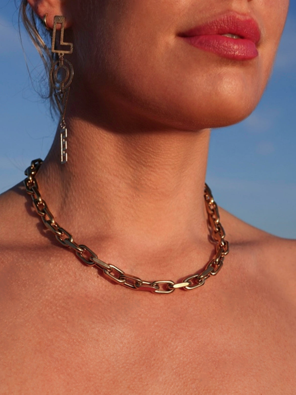 Close-up of a model wearing a millie madness gold chain necklace against a blue sky
