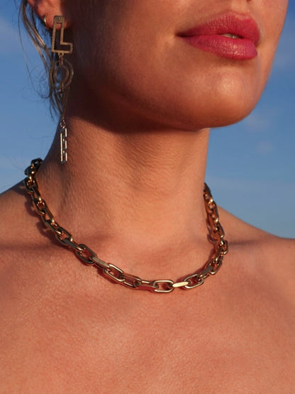 Close-up of a model wearing a millie madness gold chain necklace against a blue sky