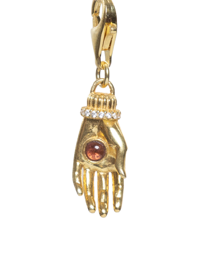 Gold charm shaped like a hand with a brown gemstone on a white background