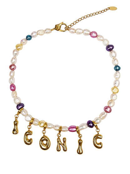 A gold-tone beaded MILLIE MADNESS necklace with white baroque pearls, small multicolor beads, and dangling gold letters spelling 'ICONIC' on a plain white background.