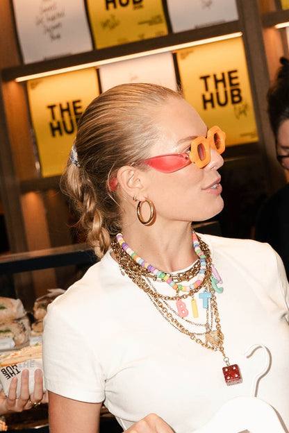 A woman in a white t-shirt wearing lots of millie madness jewelry and the bitch necklace