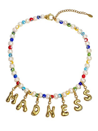 A beaded statement necklace featuring white faux pearls, colorful evil eye beads, and gold letter charms spelling MILLIE MADNESS 'MADNESS' on a white background.
