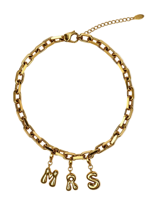 A gold-colored chunky chain MILLIE MADNESS necklace with three dangling letter charms spelling 'MRS' in a cursive font, displayed on a clean white background.