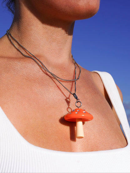 Person wearing a necklace with a orange mushroom pendant against a blue sky.