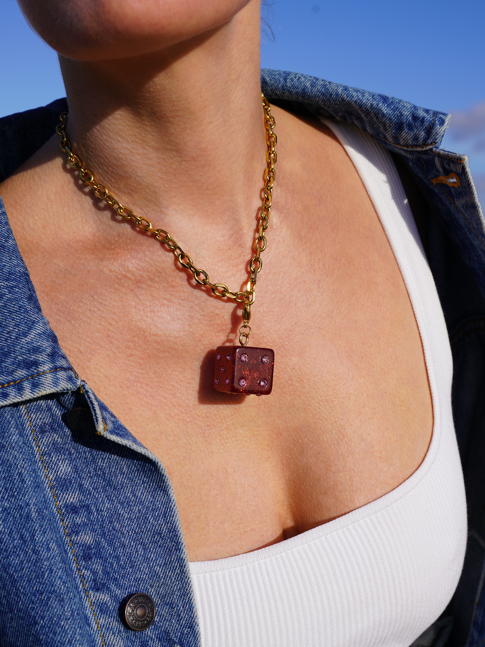 Necklace with a red dice charm worn by a person against a blue sky.