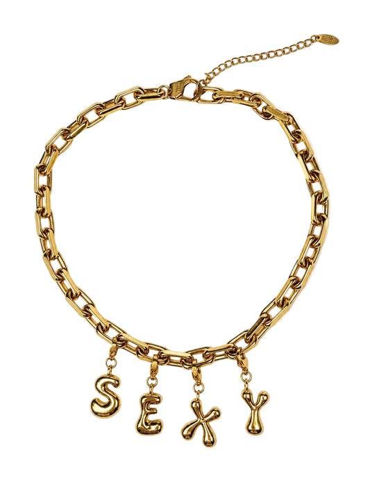 A gold-toned chunky chain MILLIE MADNESS stainless steel necklace with dangling letters spelling 'SEXY' on a plain white background.