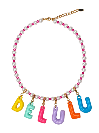 A beaded millie madness necklace featuring white real pearls and bright pink beads, with gold-tone chain hardware and dangling colorful letter charms spelling 'DELULU' in yellow, mint green, pink, purple, orange, and blue.