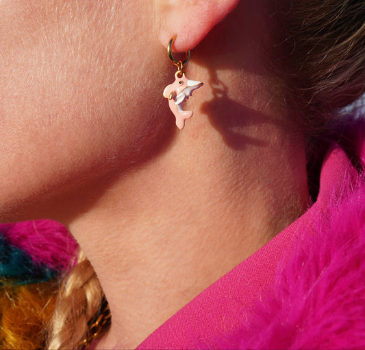 Close-up of an ear wearing a gold earring with a dolphin design.
