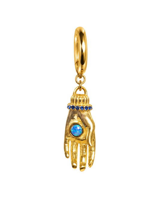 A gold Hamsa hand millie madness charm pendant featuring a central blue opal-like stone and a row of small blue stones at the wrist, suspended from a gold ring on a plain white background.
