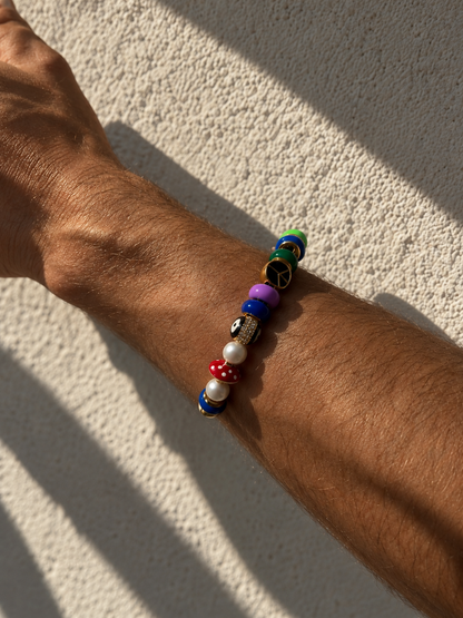 A multicolor beaded MILLIE MADNESS Bracelet worn on a person's wrist, photographed outdoors against a textured beige wall with strong natural shadows.