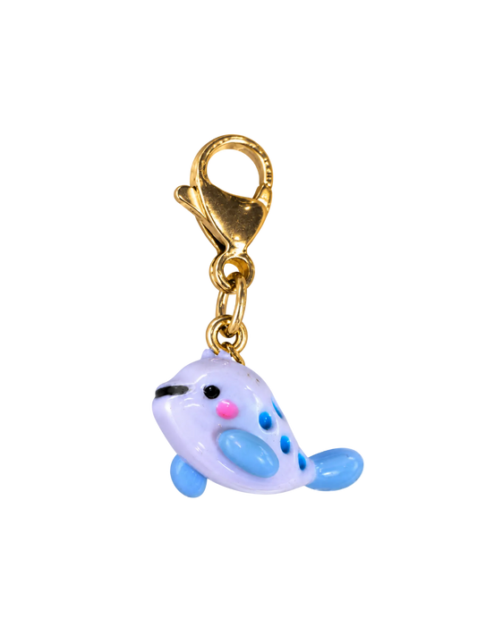 A small whale-shaped charm with a gold lobster clasp, featuring a pale lavender body, light blue flippers and spots, and pink and black facial details, isolated on a white background.